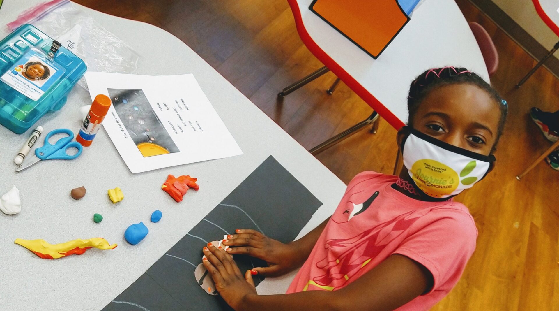 A young girl wearing a mask receives scholarship support in a classroom.