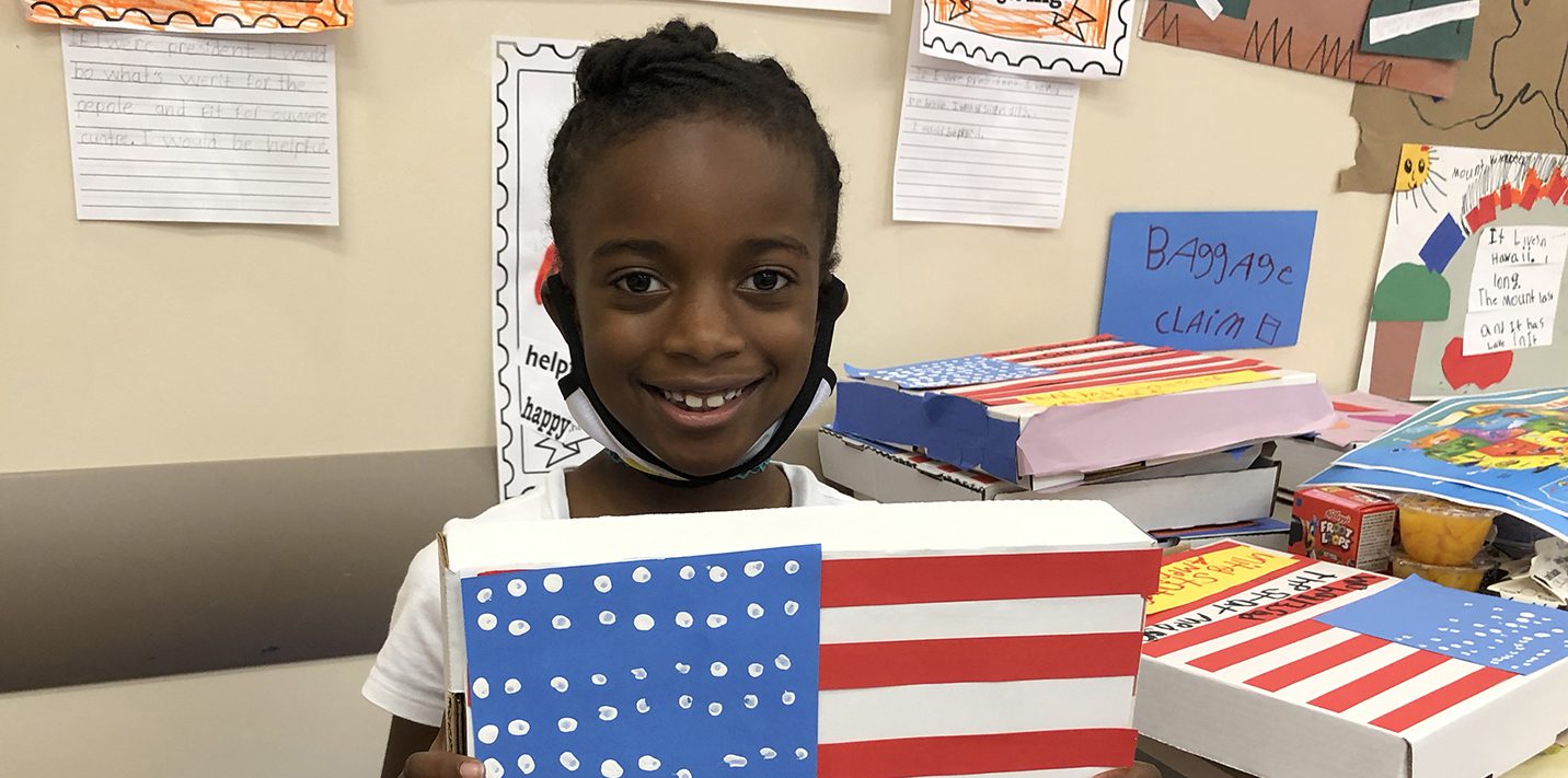 A young girl proudly holding up a box adorned with an American flag, symbolizing scholarship support.