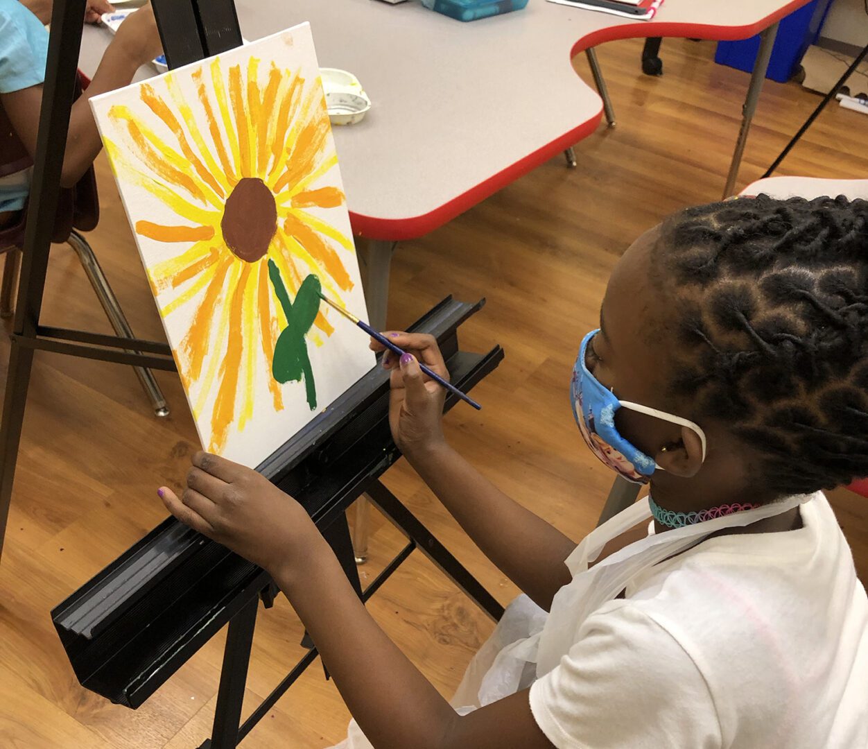 A girl wearing a face mask passionately paints a sunflower, symbolizing hope and resilience in these trying times.