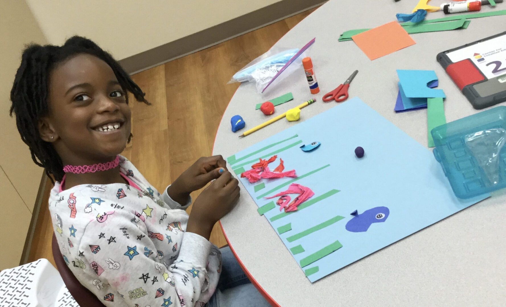 A young girl sitting at a table making crafts, enjoying scholarship support.