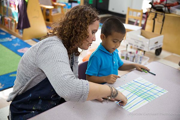 A woman working with a child at a table in a classroom.