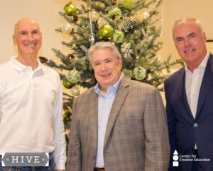 Three men standing in front of a Christmas tree, forming a jovial hive of holiday cheer.