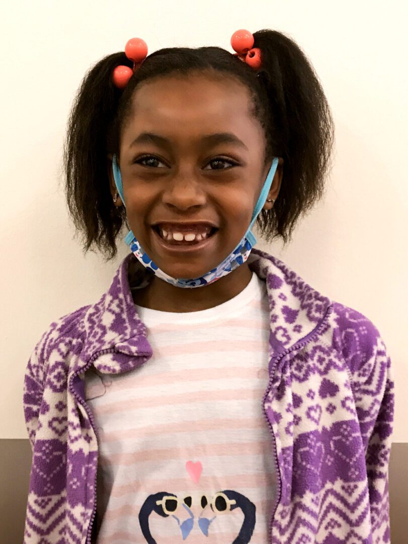 A young girl demonstrating creativity in education with her purple jacket and hat.