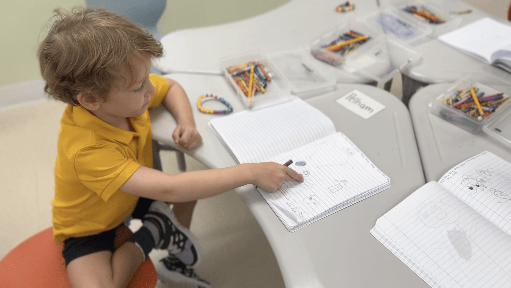 A young boy at the center for creative education, sitting at a table surrounded by crayons and pencils.