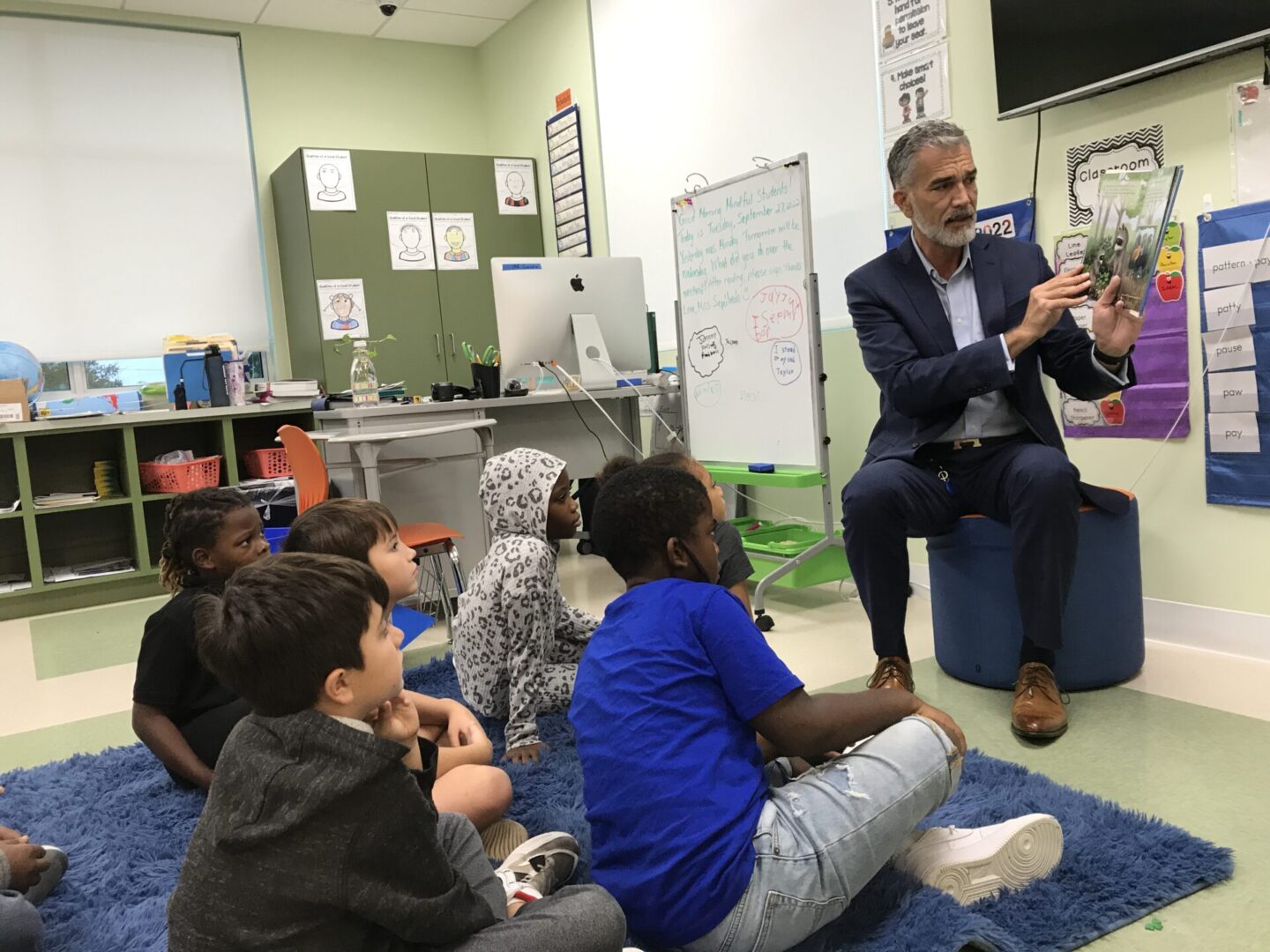 A man in a suit is engaging in a heartwarming year-end appeal as he reads to children in a classroom.