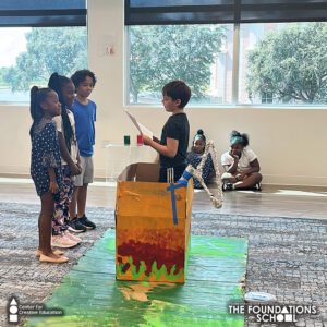 A group of second grade children standing in front of a box during their play.