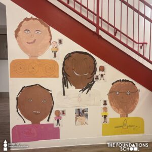 A group of children's self-portraits on a wall next to a staircase.