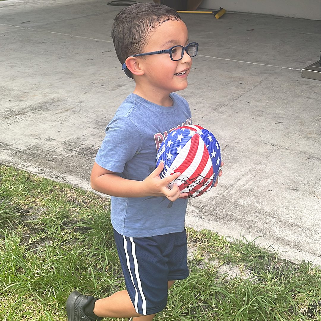 A young boy with glasses playing in a playground and holding a soccer ball.