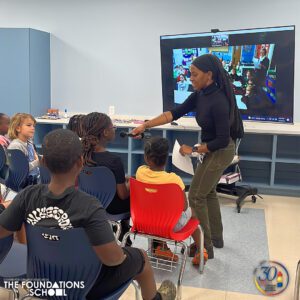 A woman is leading a global collaborations class of children in a classroom.