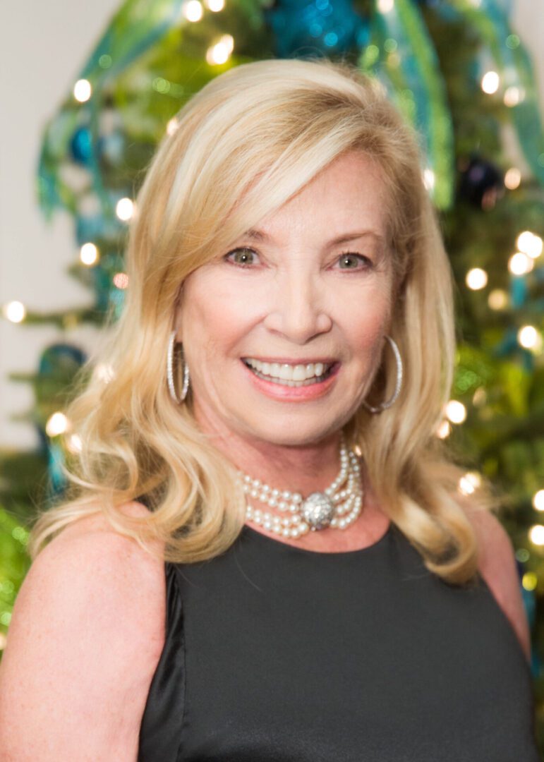 A woman in a black dress smiling in front of a Christmas tree, embracing opportunities to give.