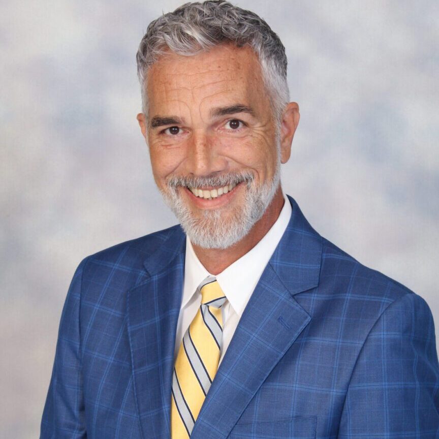 Smiling man in a blue plaid suit and yellow tie.