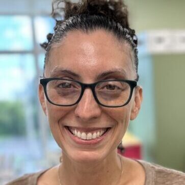 A smiling faculty member wearing glasses and a tan shirt.