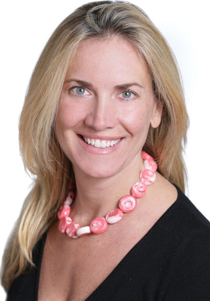 A smiling woman wearing a pink necklace is seen among a board of directors.