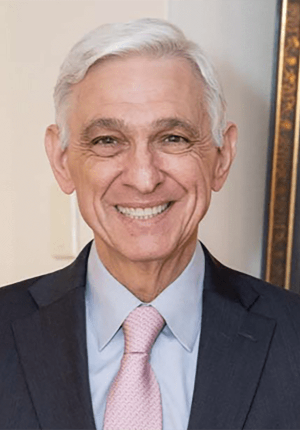 A man in a suit and tie, who seems to be a member of the board of directors, smiles in front of a painting.