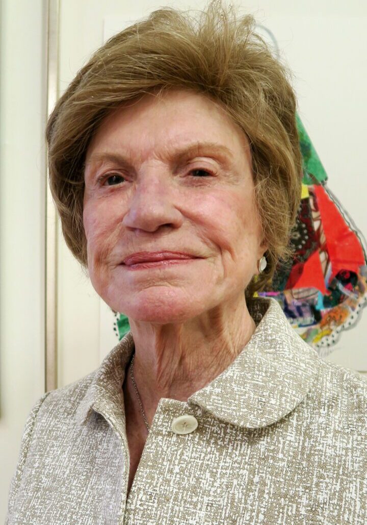 An older woman smiling in front of a painting, possibly as a member of the board of directors.