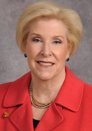 A woman in a red jacket smiling, possibly a member of a board of directors.