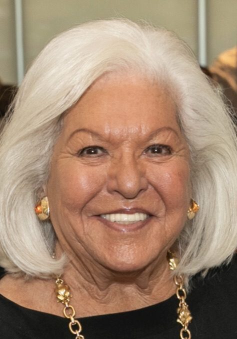 Smiling woman with white hair and gold jewelry.