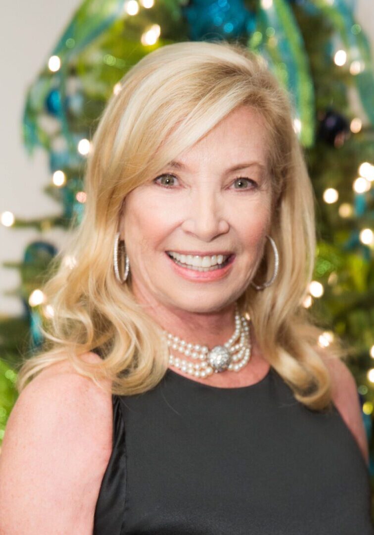 Woman with blonde hair smiling near a Christmas tree.